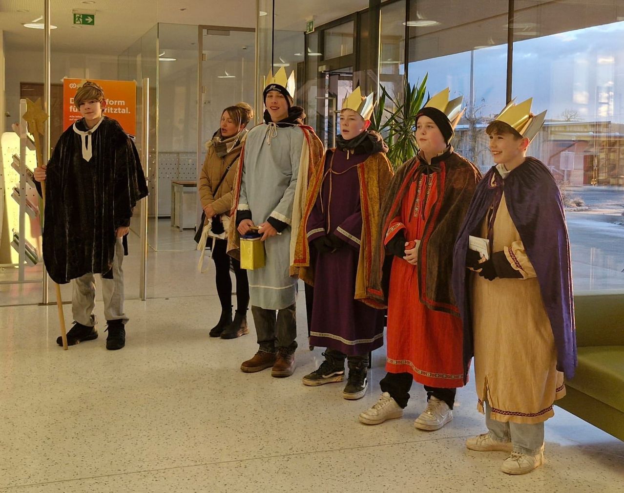 Eine Gruppe von Kindern in mittelalterlichen Kostümen, einschließlich Kronen, steht zusammen in einem Flur. Sie scheinen für ein Foto zu posieren.