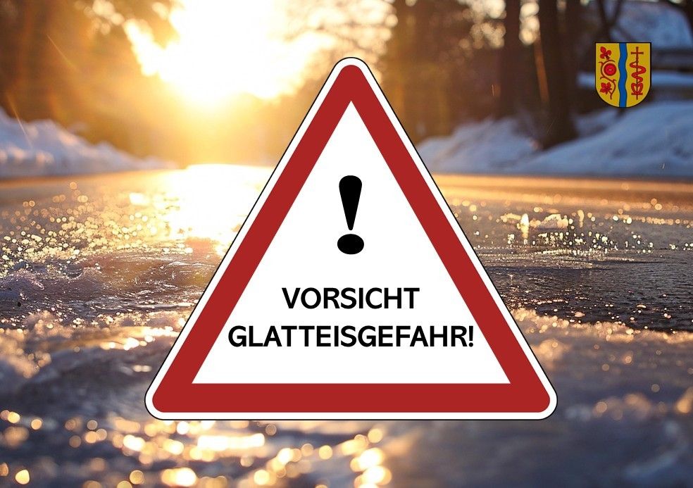Ein Warnschild auf einer verschneiten Straße zeigt 'Glatteisgefahr' mit einem aufgehenden Sonnenschein im Hintergrund.