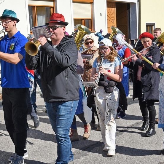 Eine Gruppe von Musikern zieht in einem Umzug, einige tragen Hüte, Brillen und Schuhe, und sie spielen verschiedene Musikinstrumente.