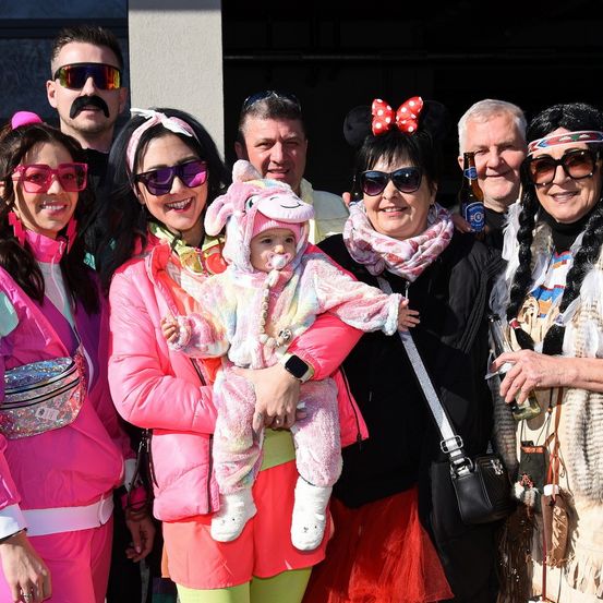 Eine Gruppe von Menschen in verschiedenen Kostümen, darunter eine Frau, die ein Baby in einem rosa Einhorn-Outfit hält, posiert für ein Foto.