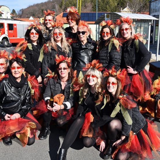 Gruppe von Frauen in roten und schwarzen Tüllröcken mit roten Blättern auf dem Kopf, posiert für ein Foto auf der Straße.