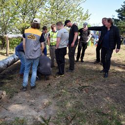 Gruppe von Arbeitern und Vorarbeitern auf einer Baustelle. Ein Arbeiter beugt sich nach unten, während andere zuschauen, und ein Mann zeigt auf etwas.