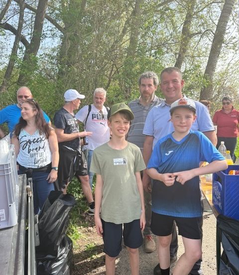 Gruppe von Menschen, die in einem Wald stehen, zwei Jungen vorne mit grünen und blauen Shirts, andere in Freizeitkleidung, lächeln und in die Kamera schauen.