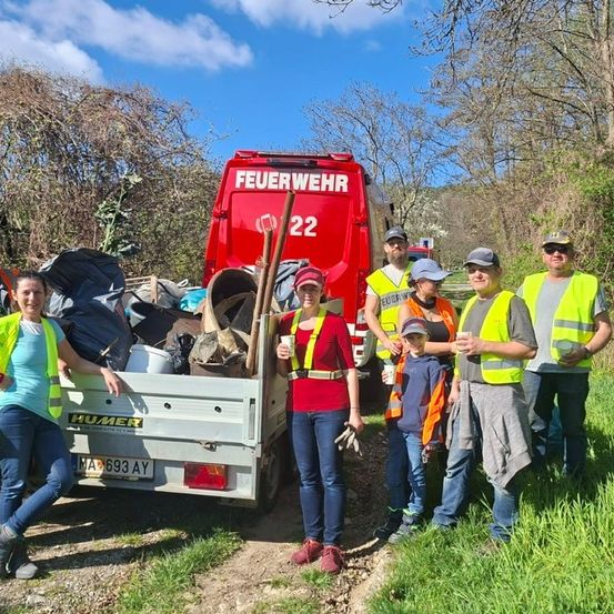 Eine Gruppe von Freiwilligen steht hinter einem roten Feuerwehr-LKW mit der Aufschrift 'Feuerwehr 22' und sammelt Müll.
