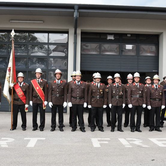 Eine Gruppe von Feuerwehrleuten in Uniformen und Helmen steht in einer Reihe vor einer Feuerwache.