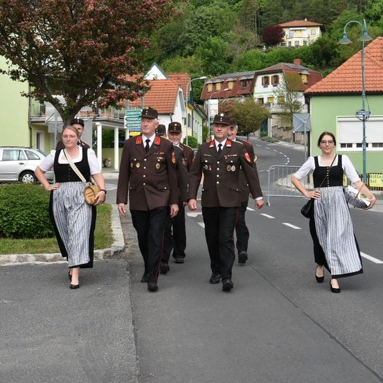 Eine Gruppe von Menschen, darunter Militäroffiziere und Frauen in traditionellen Kleidern, geht in einer Stadt eine Straße entlang.