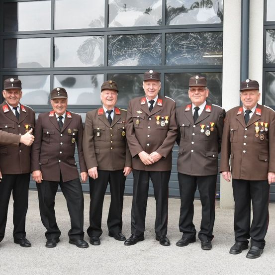 Fünf ältere Männer in identischen braunen Uniformen mit Medaillen stehen in einer Reihe vor einem Gebäude.