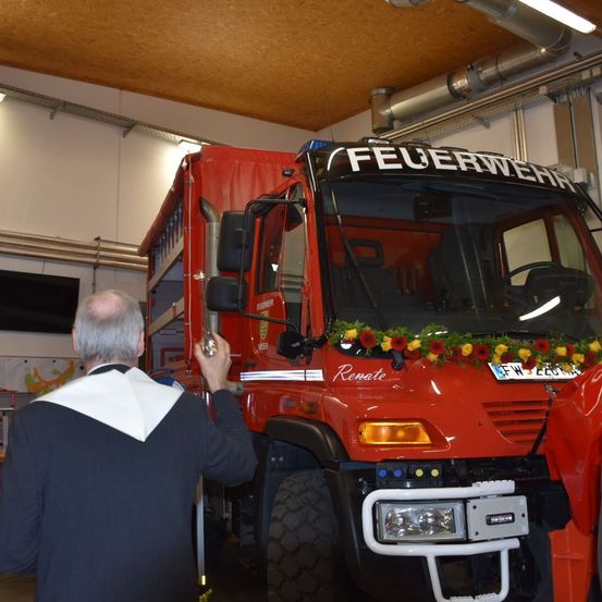 Ein Mann inspiziert einen Feuerwehrwagen namens Renate, der mit Blumen geschmückt ist, in einer Garage.