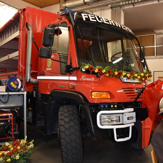 Ein roter Feuerwehrwagen namens Renate steht in einer Garage. Er hat Blumen auf der Vorderseite und ein Nummernschild.