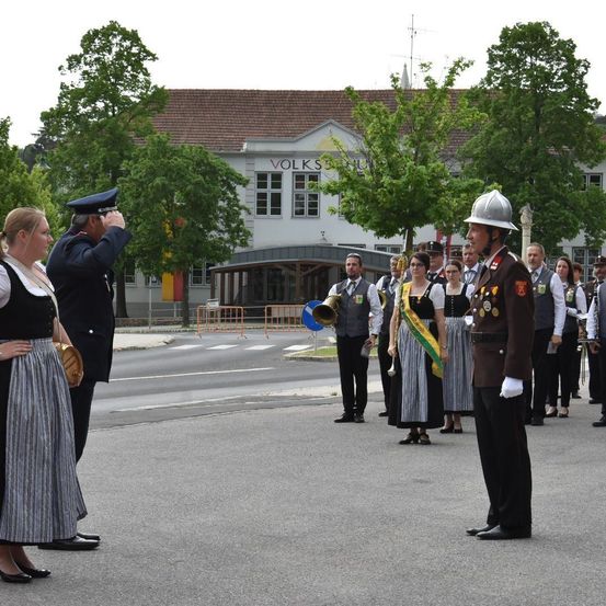 Eine Gruppe von Menschen, darunter ein Mann in Uniform, steht in einer Reihe, möglicherweise bei einer Parade, vor einem Gebäude mit der Aufschrift Volks.