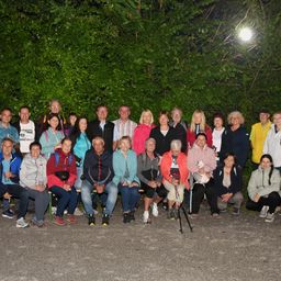 Eine Gruppe von Menschen posiert nachts für ein Foto. Sie sitzen und stehen vor einigen Bäumen.