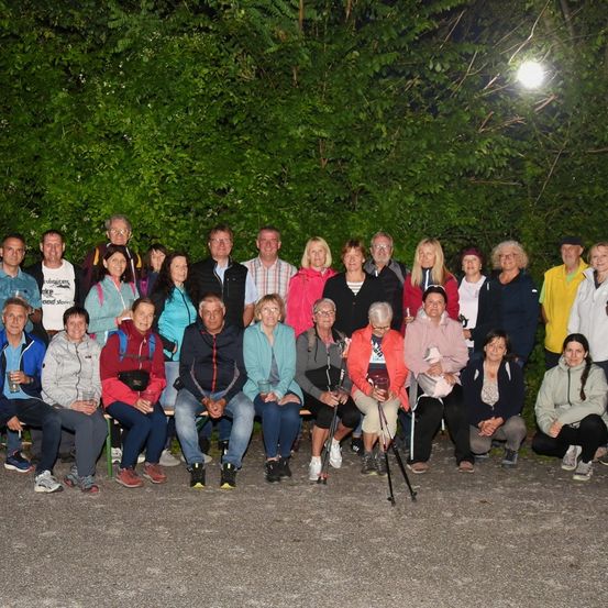 Eine Gruppe von Menschen posiert nachts für ein Foto. Sie sitzen und stehen vor einigen Bäumen.