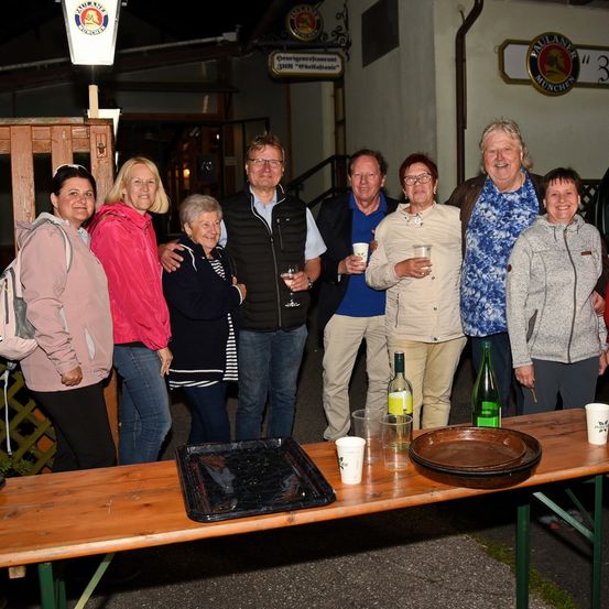 Eine Gruppe Erwachsener steht nachts vor einem Gebäude und posiert für ein Foto mit Getränken in der Hand.