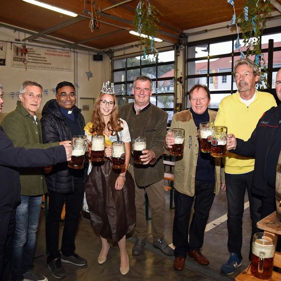 Eine Gruppe von Menschen steht in einem Raum und hält Bierkrüge. Sie scheinen ein Ereignis zu feiern. Einer von ihnen ist eine Frau mit einer Krone. Sie lächeln und posieren für ein Foto.