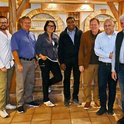 Eine Gruppe von Menschen steht zusammen in einem Raum und lächelt für ein Foto. Ein Schild mit der Aufschrift 'WETZONR' befindet sich über ihnen.