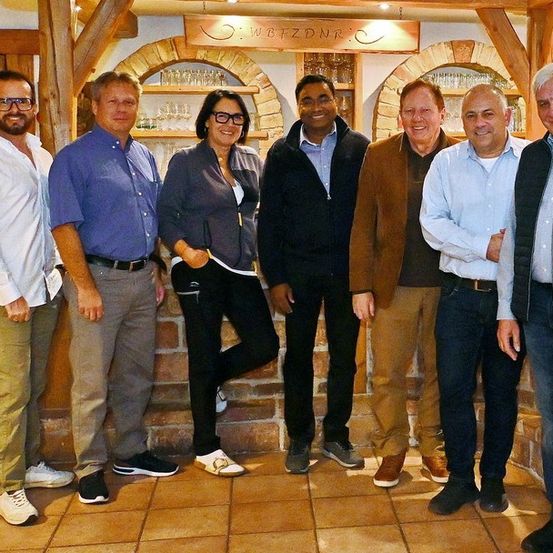 Eine Gruppe von Menschen steht zusammen in einem Raum und lächelt für ein Foto. Ein Schild mit der Aufschrift 'WETZONR' befindet sich über ihnen.