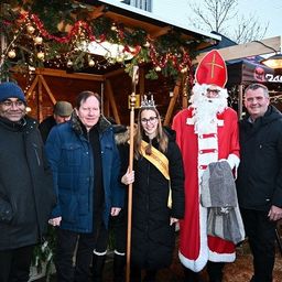 Eine Gruppe von Menschen posiert für ein Foto vor einem festlich geschmückten Haus. Unter ihnen ist ein Mann als Weihnachtsmann verkleidet, der einen Stab hält.