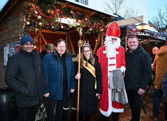 Eine Gruppe von Menschen posiert für ein Foto vor einem festlich geschmückten Haus. Unter ihnen ist ein Mann als Weihnachtsmann verkleidet, der einen Stab hält.