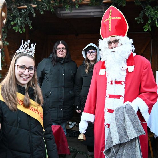Eine Gruppe von Menschen, darunter eine Frau mit Krone, posiert für ein Foto mit einem Mann, der als Sankt Nikolaus verkleidet ist.