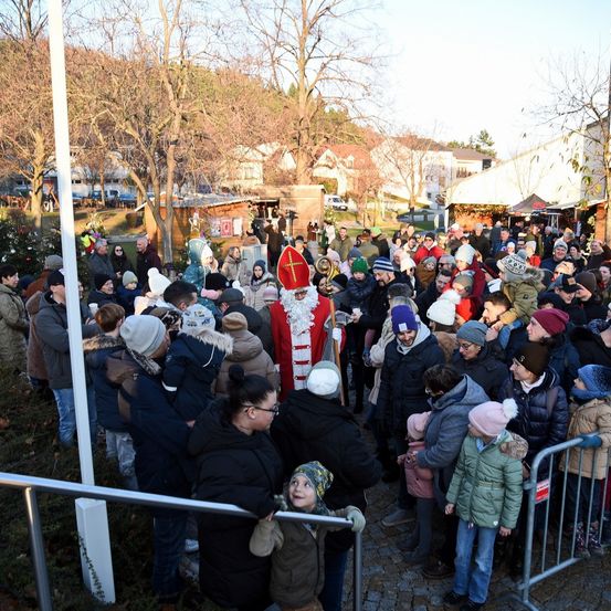 Eine Menschenmenge in Winterkleidung versammelt sich um einen Mann, der als Weihnachtsmann gekleidet ist und hinter einem Metallzaun steht.