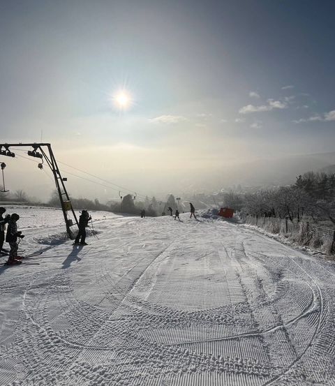 Eine Skipiste mit mehreren Skifahrern und einer Skilift im Hintergrund. Der Himmel ist blau mit einigen Wolken.