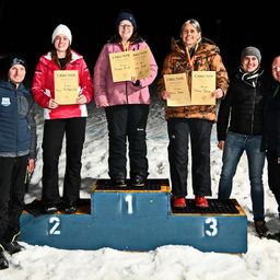 Fünf Personen stehen auf einem verschneiten Podest, wobei die Drittplatzierte rechts steht. Die Erstplatzierte hält ein Zertifikat, ebenso wie die Zweit- und Drittplatzierte.