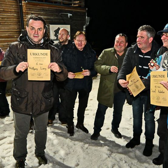 Eine Gruppe von Männern steht im Schnee, jeder hält ein Zertifikat. Der Mann in der Mitte hält ein Zertifikat für Wolfgang Lang. Die Männer sind in Jacken und Hosen gekleidet und scheinen sich in guter Stimmung zu befinden.