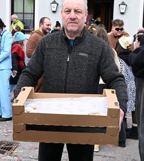 Ein Mann hält eine Schachtel Donuts vor einem Gebäude mit dem Schild Treffpunkt Kondi. Menschen sind draußen versammelt.