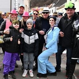 Eine Gruppe von Erwachsenen und Kindern in Kostümen posiert für ein Foto auf einer Straße während einer Veranstaltung.