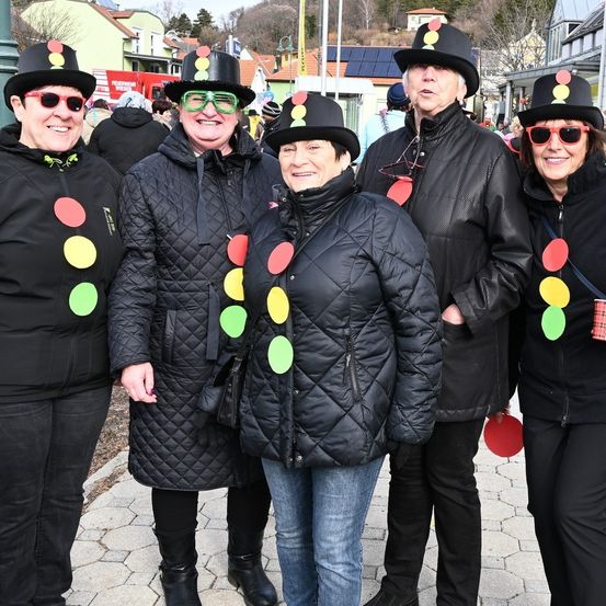 Fünf Frauen stehen eng beieinander und tragen schwarze Hüte mit Ampeldekorationen und Sonnenbrillen. Sie lächeln und scheinen für ein Foto zu posieren.