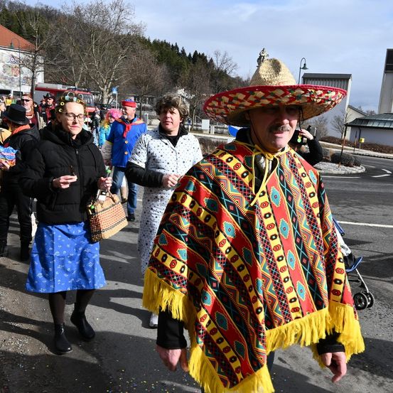 Menschen in Kostümen gehen auf der Straße, einer trägt einen Sombrero. Sie nehmen wahrscheinlich an einer Parade teil.