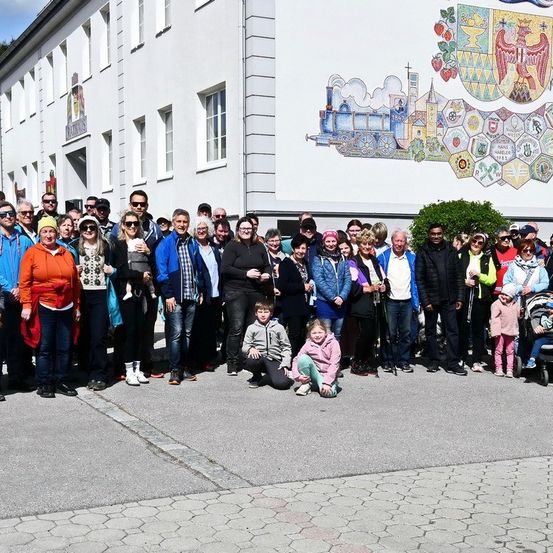 Eine Gruppe von Menschen, einschließlich Kindern, posiert für ein Foto vor einem Gebäude mit dekorativen Wandgemälden an der Seite.
