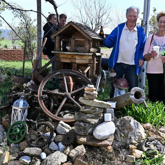 Eine Familie steht vor einer Sammlung rustikaler Gegenstände, einschließlich eines Holzrades und einer Steinmauer.