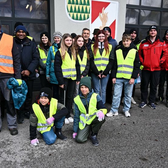 Eine Gruppe von Freiwilligen in Warnwesten posiert für ein Foto vor einem Gebäude. Sie tragen Winterkleidung und Handschuhe. Das Gebäude hat ein Logo an der Wand.