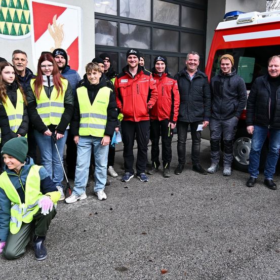 Eine Gruppe von Menschen in Sicherheitswesten und Winterkleidung steht vor einem Feuerwehrauto auf einem Parkplatz.