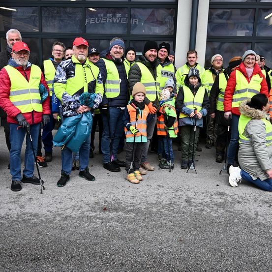 Eine Gruppe von Menschen in Sicherheitswesten und Mützen steht zusammen vor einem Gebäude. Einige halten Skistöcke und andere tragen Taschen. Ein Kind kniet im Vordergrund.