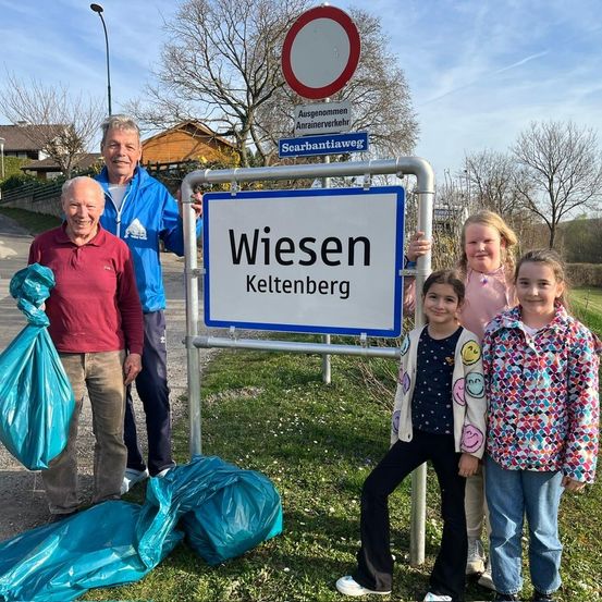 Eine Gruppe von Menschen steht neben einem Schild mit der Aufschrift Wiesen Kelttenberg. Zwei von ihnen halten Mülltüten. Der Mann in Blau hält das Schild.