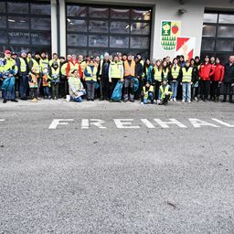 Eine Gruppe von Menschen in gelben Westen und Mützen steht in einer Reihe vor einem Gebäude. Auf dem Boden steht das Wort Freihal geschrieben.