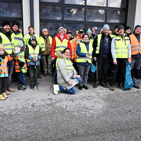 Eine Gruppe von Menschen, einschließlich Kindern, posiert für ein Foto vor einem Gebäude, alle tragen Sicherheitswesten. Einige tragen Taschen, während andere Mützen und Brillen haben.