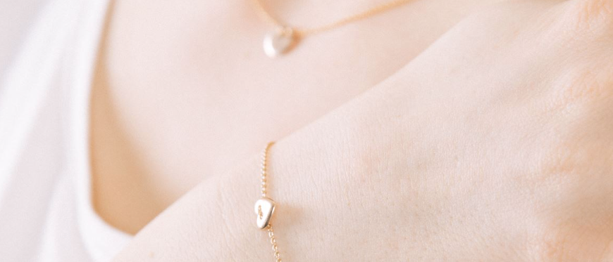 Eine Frau trägt eine goldene Kettenkette mit einem Herzanhänger und ein goldenes Kettenarmband mit einem Herzanhänger.