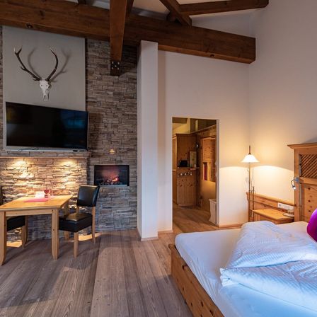Ein gemütliches Schlafzimmer mit Kamin, eingebautem Fernseher und einem Hirschschädel an der Wand. Das Bett ist ordentlich gemacht, und ein Schreibtisch mit Lampe steht daneben.