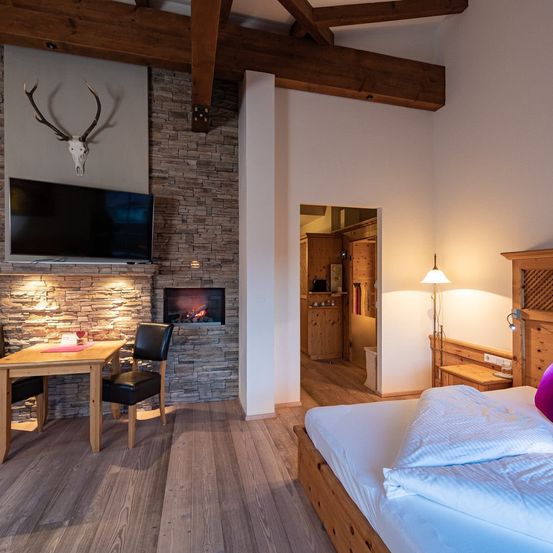 Ein gemütliches Schlafzimmer mit Kamin, eingebautem Fernseher und einem Hirschschädel an der Wand. Das Bett ist ordentlich gemacht, und ein Schreibtisch mit Lampe steht daneben.