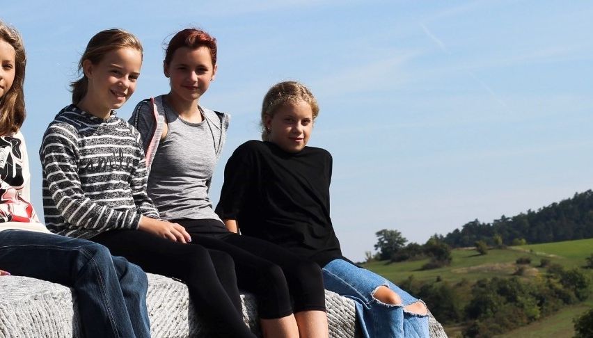 Zwei Mädchen sitzen auf einer weißen Struktur mit Blick auf ein großes kuppelförmiges Gebäude im Hintergrund.