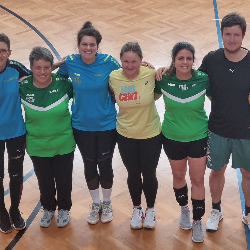 Eine Gruppe von fünf Frauen und einem Mann steht in einem Fitnessstudio und lächelt für ein Foto. Sie tragen Sportuniformen.