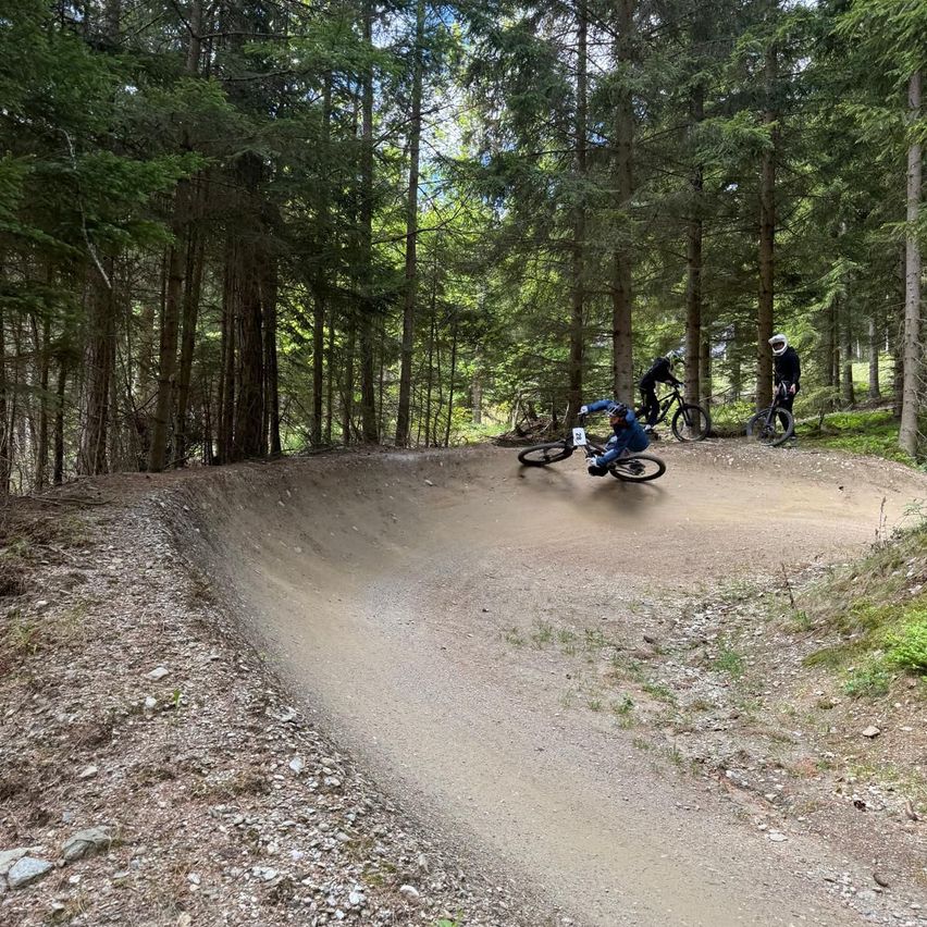 Drei Radfahrer fahren im Wald mit ihren Fahrrädern, einer von ihnen liegt am Boden, während die anderen in der Nähe des Pfades stehen.