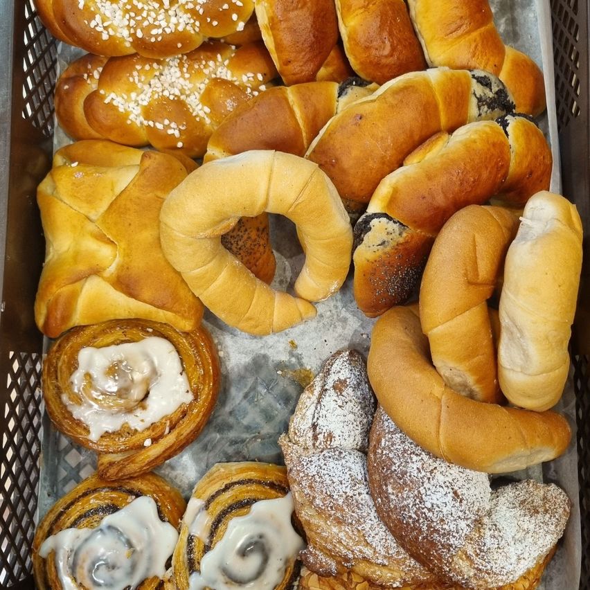 Ein Korb voller verschiedener Brotsorten, darunter Zimtschnecken, Brezeln und Bagels, alles mit Zucker oder Sesam bestreut.