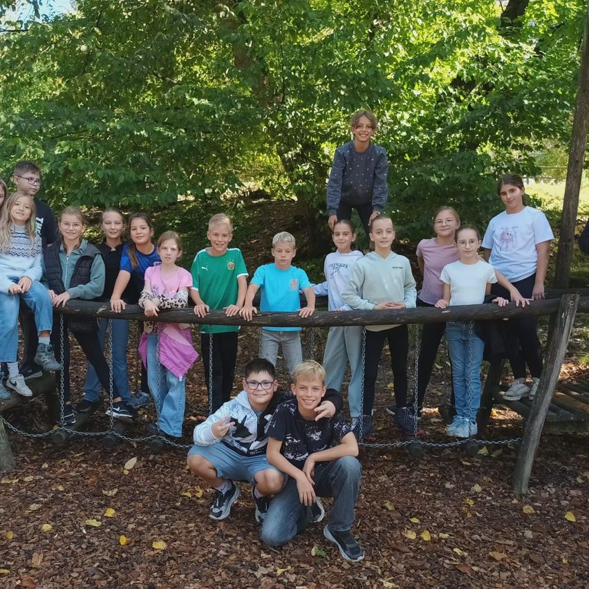 Eine Gruppe von Kindern und Jugendlichen posiert für ein Foto in einer Waldumgebung, einige stehen auf einem Holzbalken.