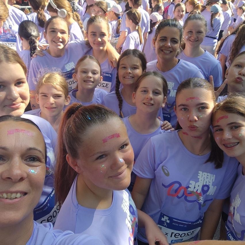 Eine Gruppe junger Frauen in Lavendelshirts, die mit Farbe im Gesicht Spaß haben. Sie lächeln für ein Selfie bei einer Veranstaltung.