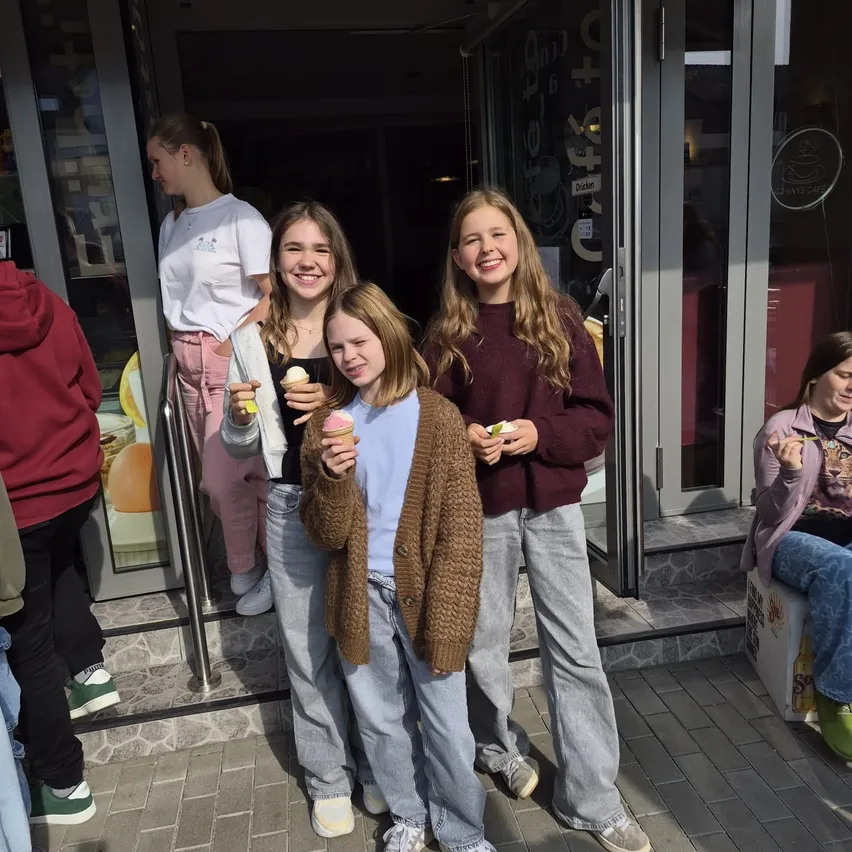 Vier Mädchen stehen vor einem Geschäft und halten Eisbecher in der Hand.