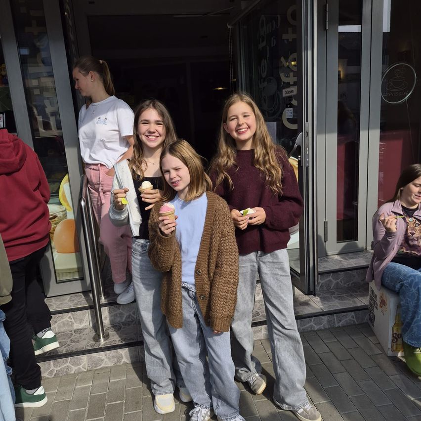 Vier Mädchen stehen vor einem Geschäft und halten Eisbecher in der Hand.